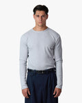 A man wearing a light gray long-sleeve crewneck shirt tucked into dark navy trousers with a black belt, photographed against a clean white studio background.